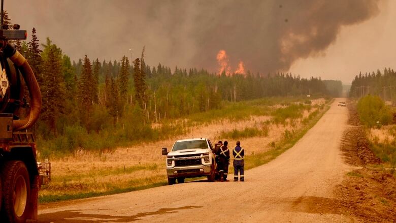 Three people look at a fire burning in the distance.