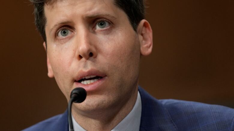 A man in a jacket and tie speaks into a microphone