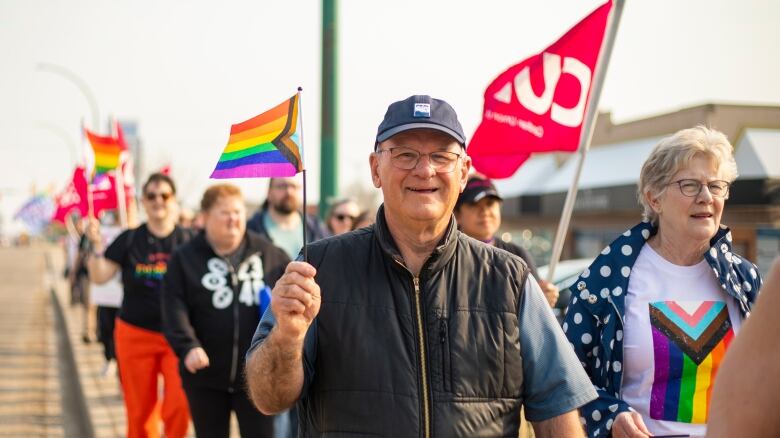 A group of around 80 people march carrying Pride and CUPE flags in support of the LGBTQ community.