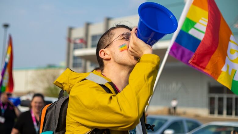 A person with a rainbow drawn on their cheek talks into a megaphone.