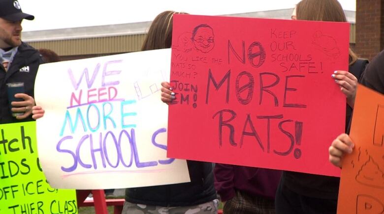 Students holding protest signs that read we need more schools and no more rats. 