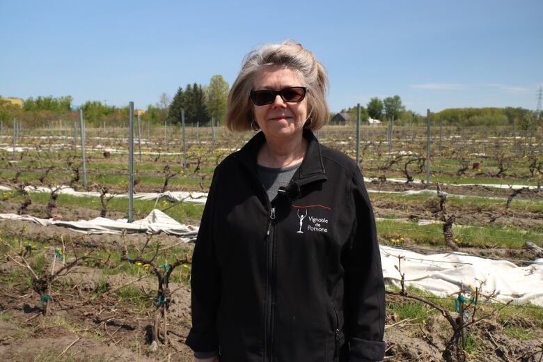 A woman stands in a vineyard.