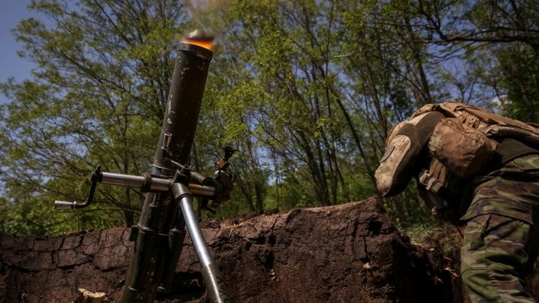 A soldier in a trench hunches over and braces themselves as a mortar fires a round.