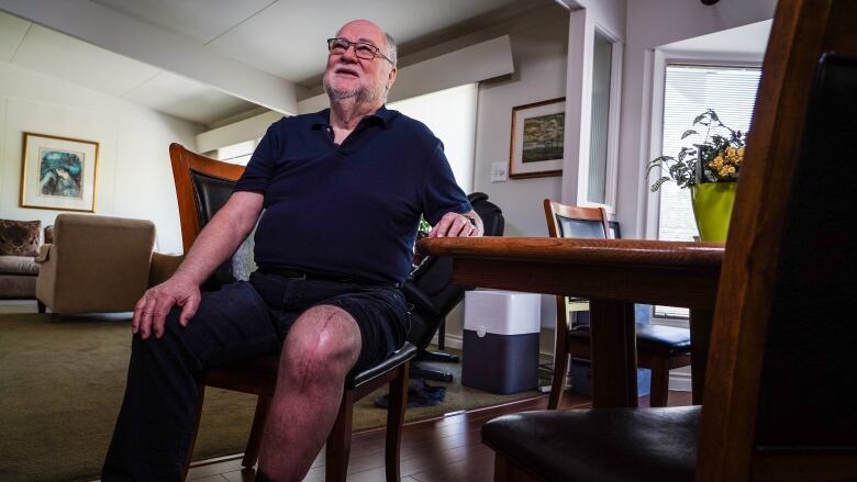 A man with a large surgical scar on his knee sits at a table.