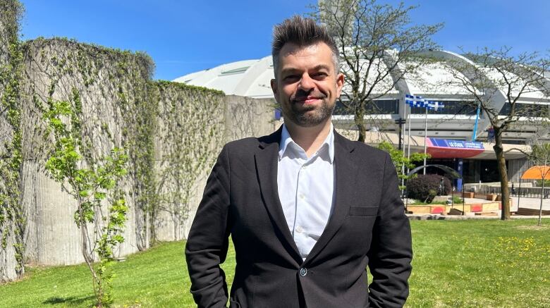 A man wearing a black blazer and salt and pepper hair stands outside Montreal's Olympic stadium.