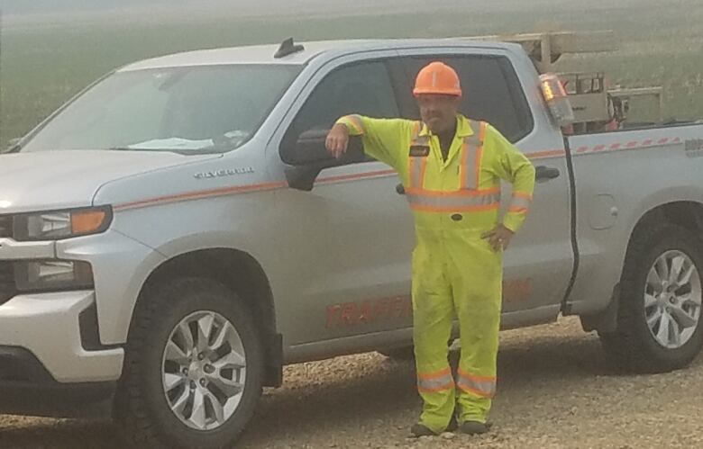 Man in construction uniform stands by truck.