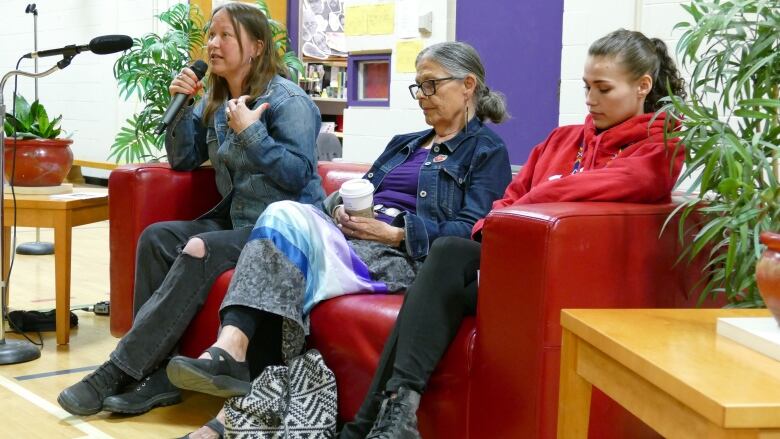 Three people sitting on a couch are pictured. One of them speaks into a microphone.