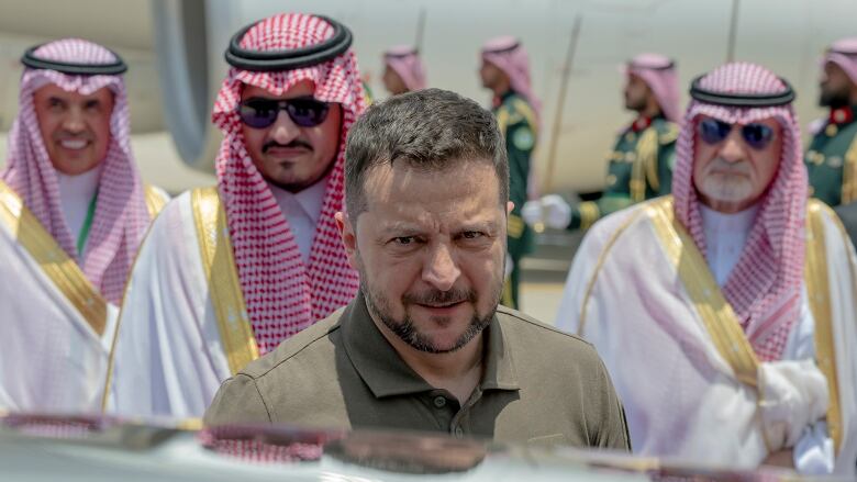 A man stands next to a car with three men behind him.