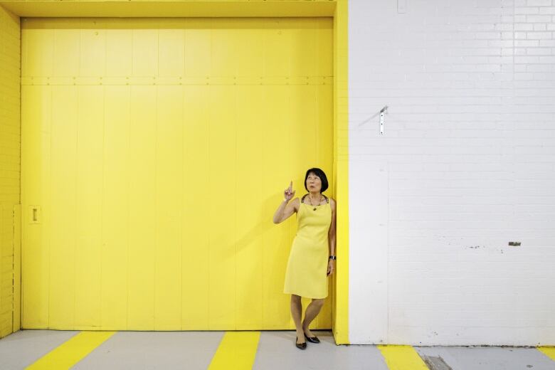 Woman in a yellow dress stands in front of a yellow warehouse door. The tone of her dress and the door match almost exactly.