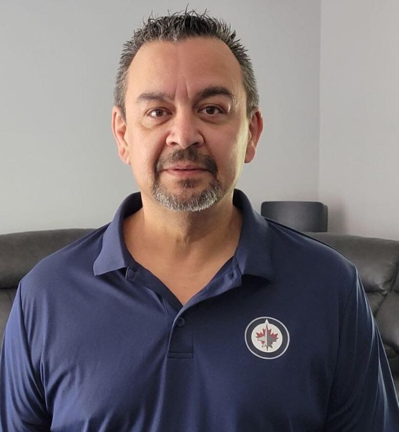 A man with short dark hair and a goatee wearing a blue Winnipeg Jets polo shirt looks at the camera.