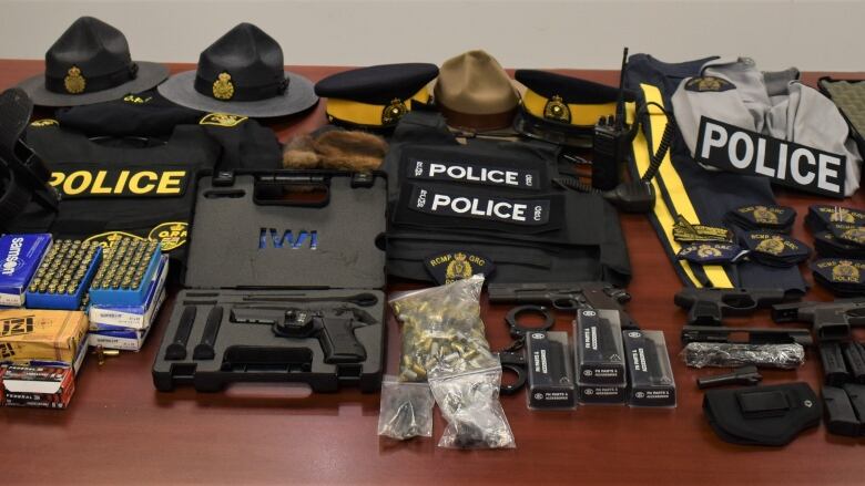 An assortment of hats and clothing, many emblazed with the word 'police,' are displayed on a table along with weapons and ammunition.