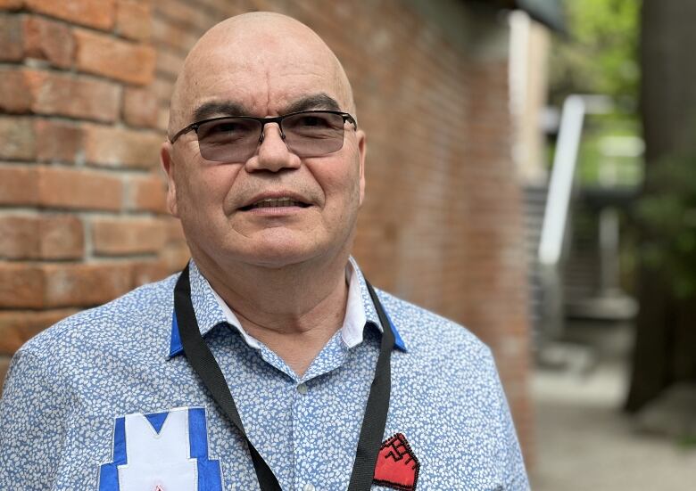 A bald man wears tinted glasses and a blue and white shirt.