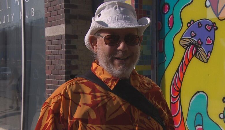 A man in a hat and sunglasses smiles toward the camera.