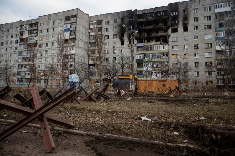 An apartment building with heavy shelling damage is shown.