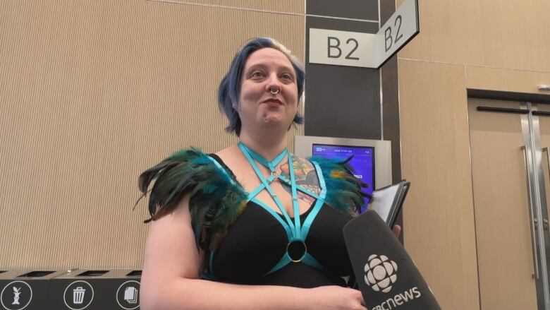 A woman with a feathered top speaks to camera.