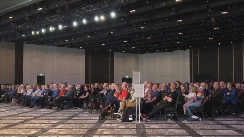 A large group of seated people in a big room look toward the stage..