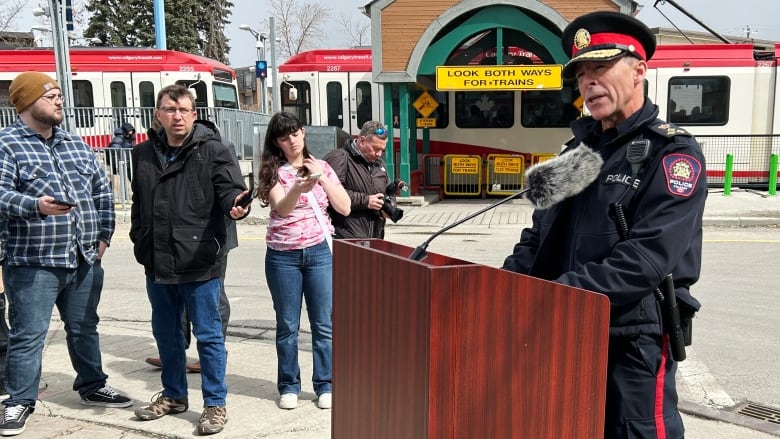 A man wearing a police hat stands behind a podium in front of a train in Calgary.