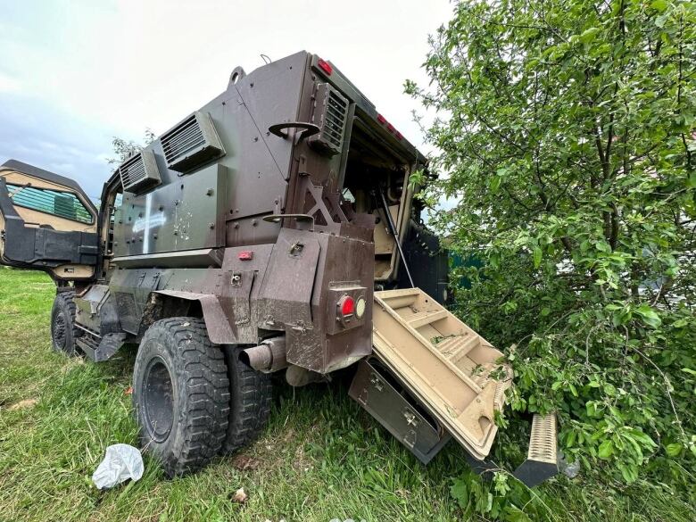 An armoured vehicle is seen abandoned near a tree.