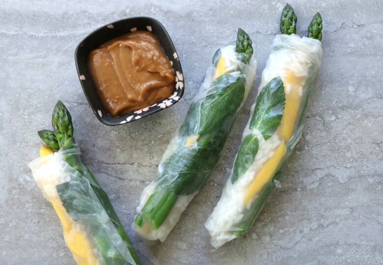 Close-up shot of asparagus and mango salad rolls accompanied by a serving of brown peanut sauce. 