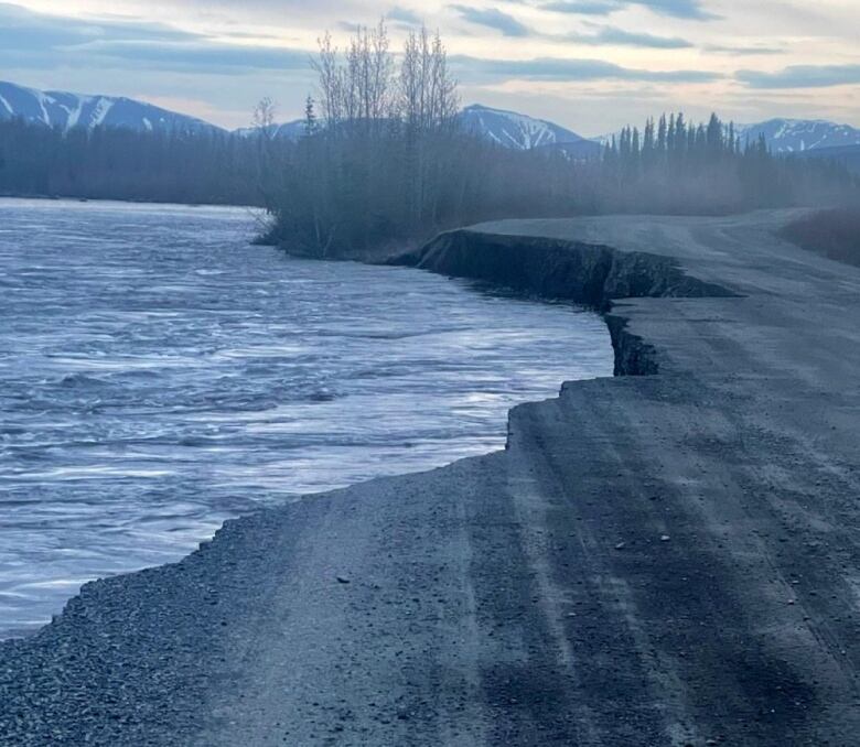 A gravel road partially washed out by a flooding river.