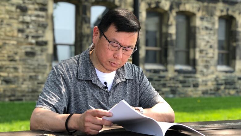 A man in a greay polo shirt reads through a report on Parliament Hill.