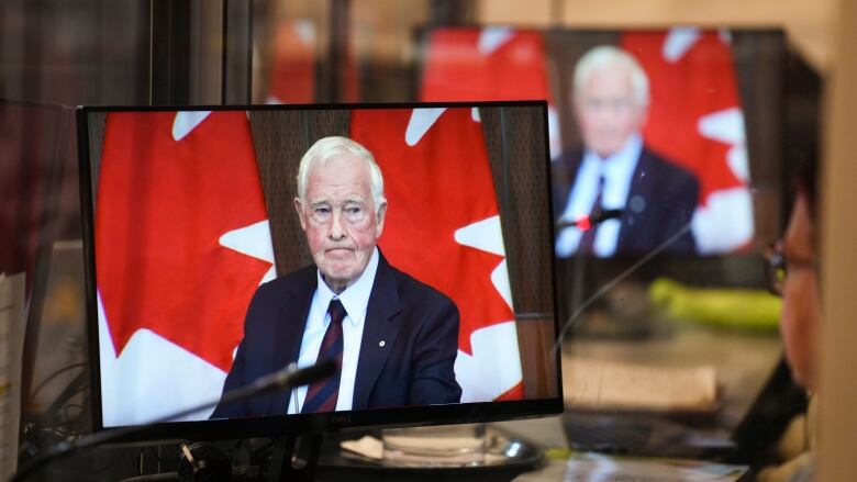 A grey-haired man is seen on multiple screens with a Canadian flag in the background.