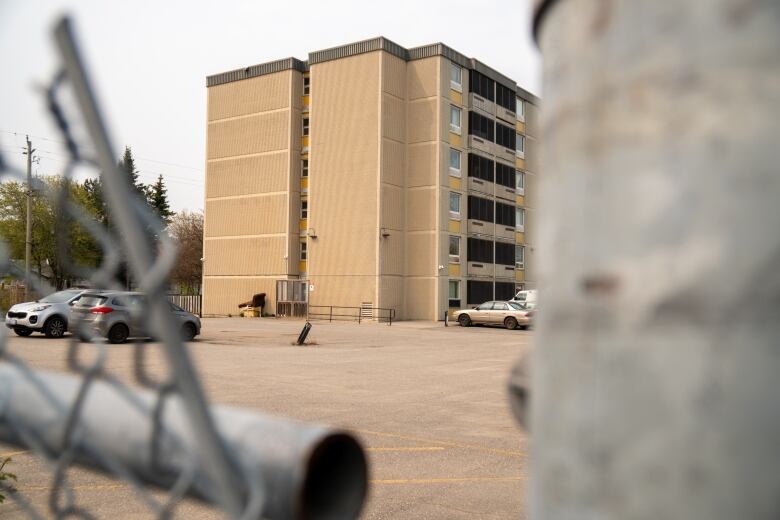 A shot of a light-coloured building framed by a chain-link fence.