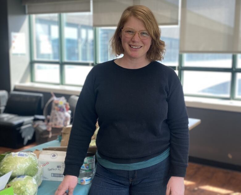 A woman smiles into the camera, with some food on a table behind her.