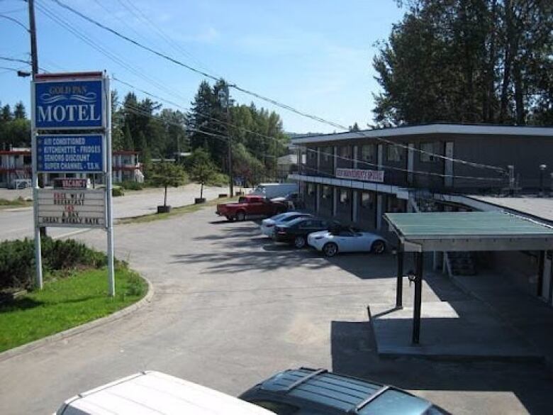 A large Gold Pan Motel sign stands above a two-storey motel and cars in the parking lot. 