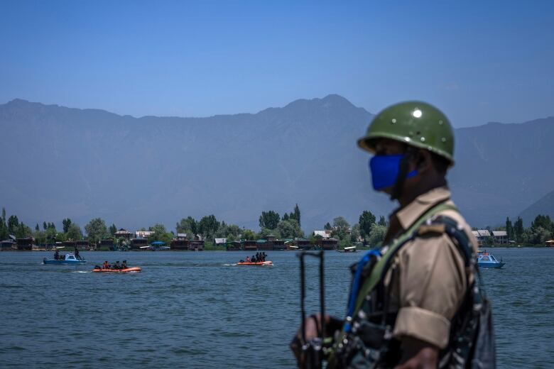 An Indian paramilitary soldier stands guard as his colleagues patrol Dal Lake ahead of G20 tourism working group meeting in Srinagar, Indian-controlled Kashmir, Saturday, May 20, 2023. Authorities have stepped up security and deployed elite commandos to prevent rebel attacks during the meeting of officials from the Group of 20 industrialized and developing nations in the disputed region next week. (AP Photo/Dar Yasin)