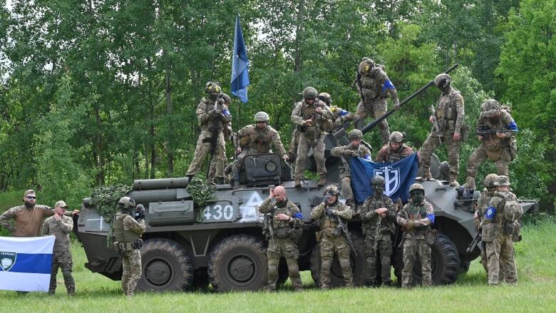 A group of men in green camouflage uniforms stand in front of and on top of a tank.