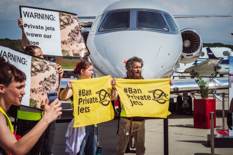 Demonstrators stand with signs protesting private jets.