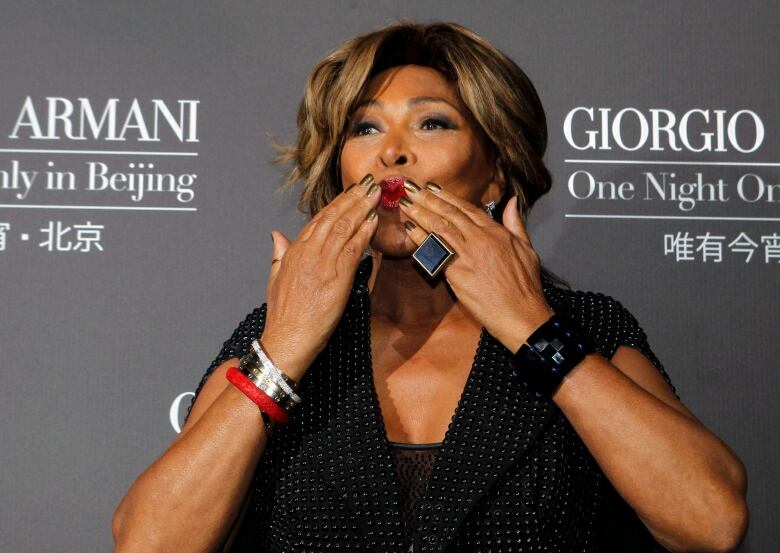 A woman standing on a red carpet blows kisses to the camera.