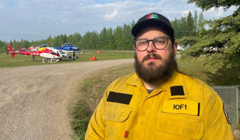 A man in a yellow uniform with two helicopters on the ground in the distance.