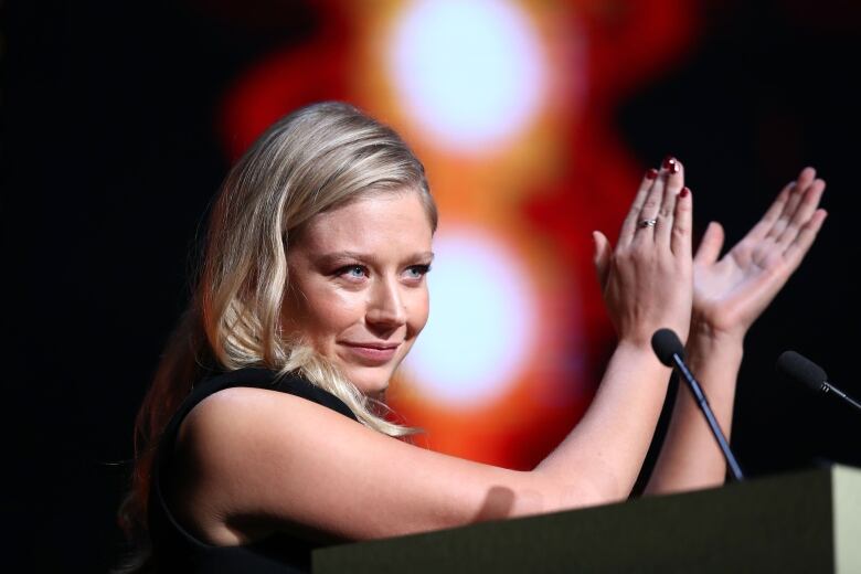 A blond woman smiles and claps. 