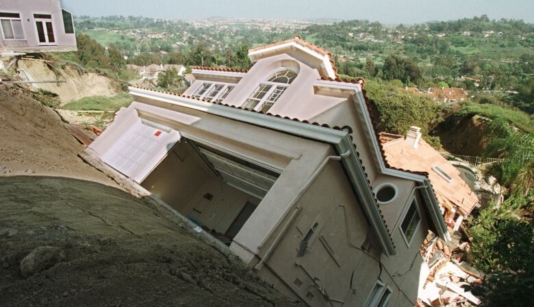 A large house slides down a muddy hill.