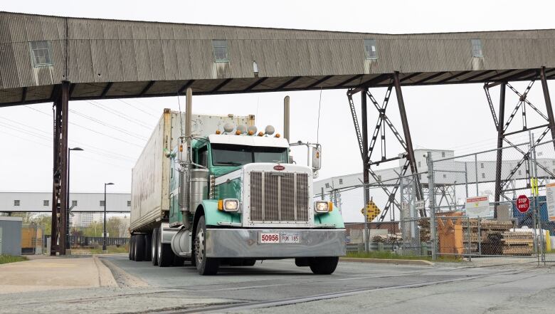 A green truck passes under a container