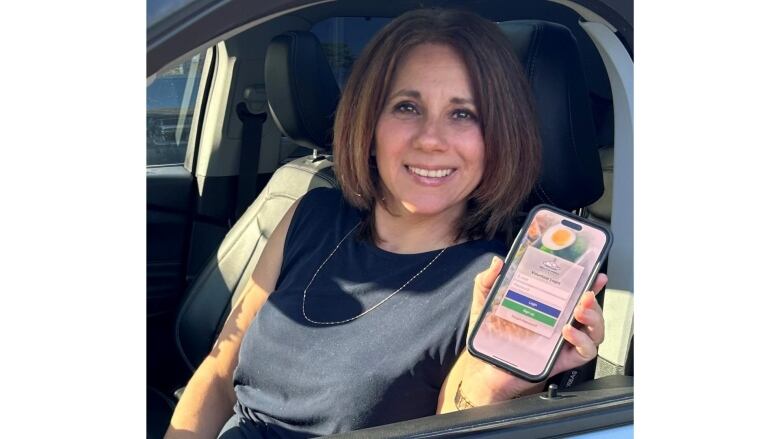 A woman sitting in a car holding a phone with an app open.