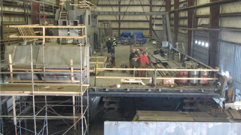 People work inside a large building with scaffolding visible in the foreground.