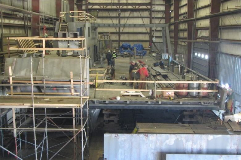 People work inside a large building with scaffolding visible in the foreground.