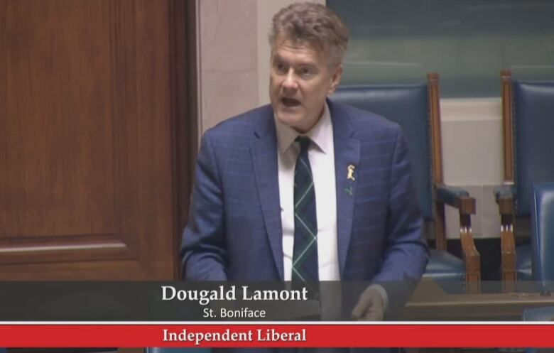 A man in a blue suit, white shirt and tie speaks in a government room.