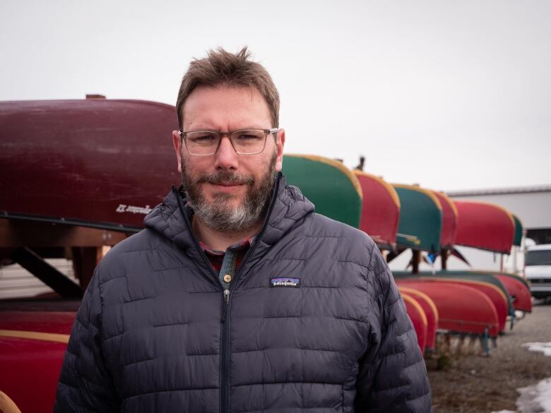 A man stands in front of a bunch of canoes on a rack.