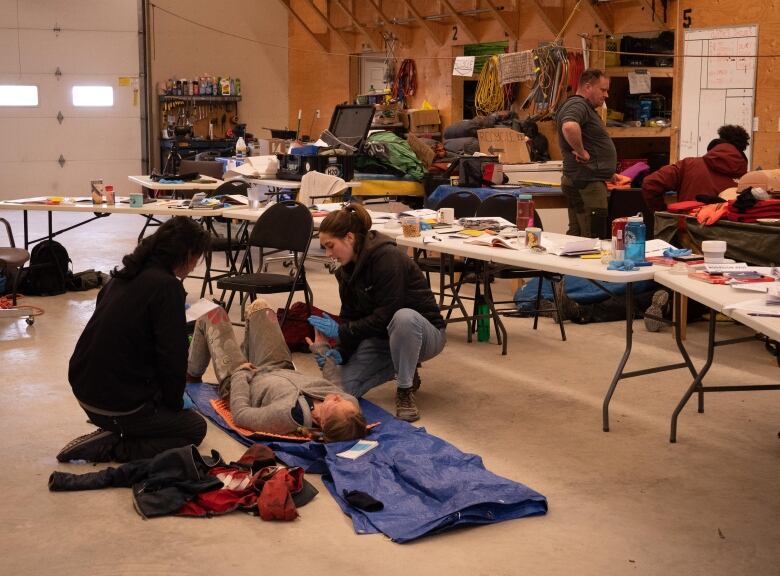 A view of a room with tables and wilderness equipment and several people engaged on training activities.