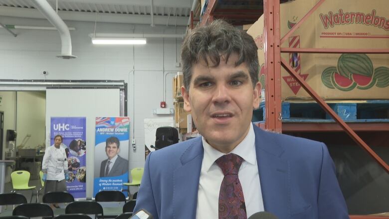 A man in a blue suit speaks in a warehouse. 