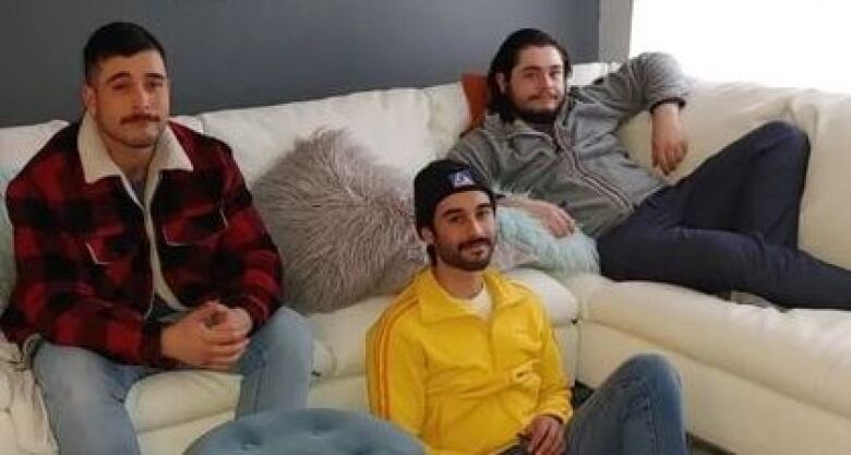 Three men sit on a sectional couch.