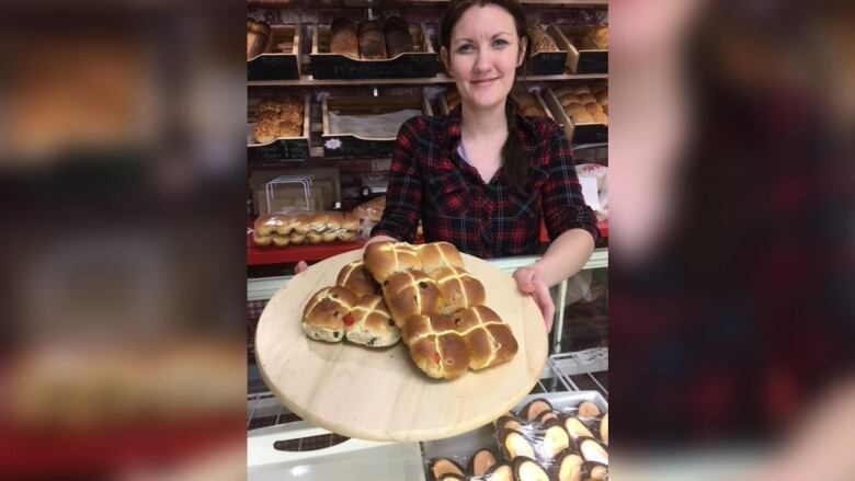 A woman holding hot cross buns in a bakery.