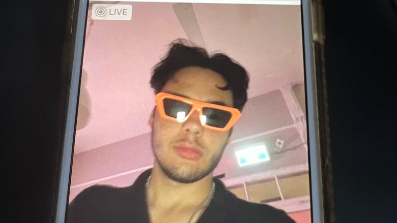 An iPhone is pictured with a photo of a man wearing bright orange sunglasses pulled up. 