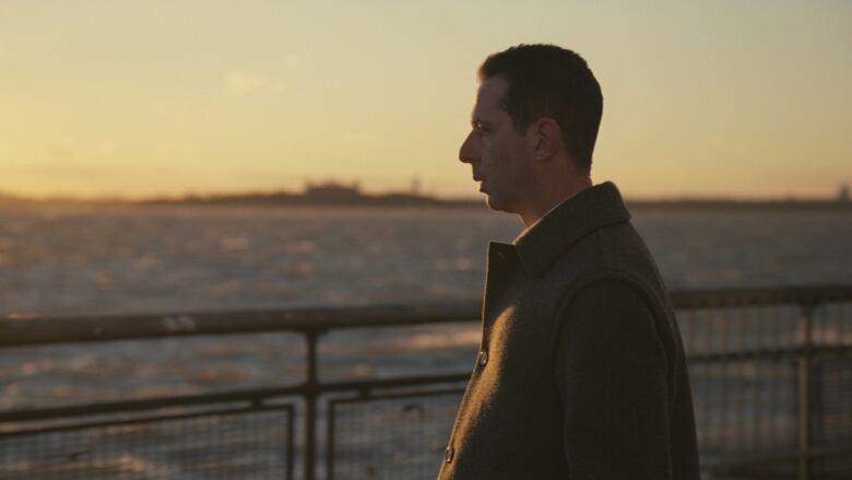 A man stands at a waterfront, looking into the distance.