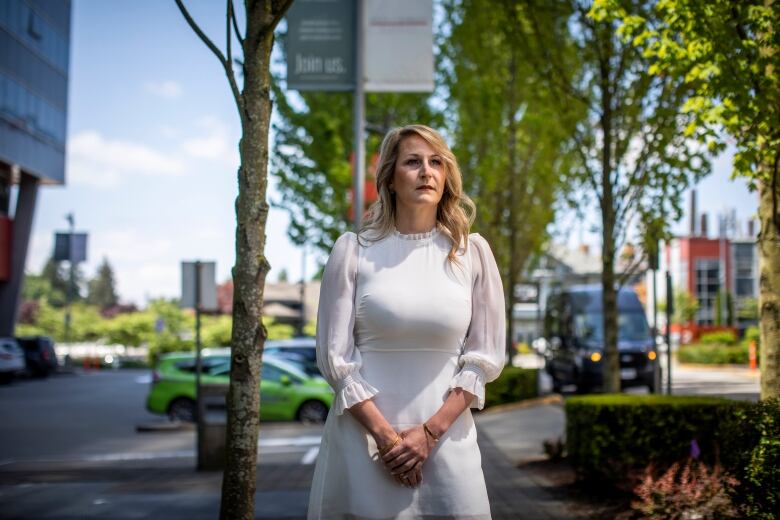 A blonde woman in a white dress is pictured outside in an urban area on a sunny day.