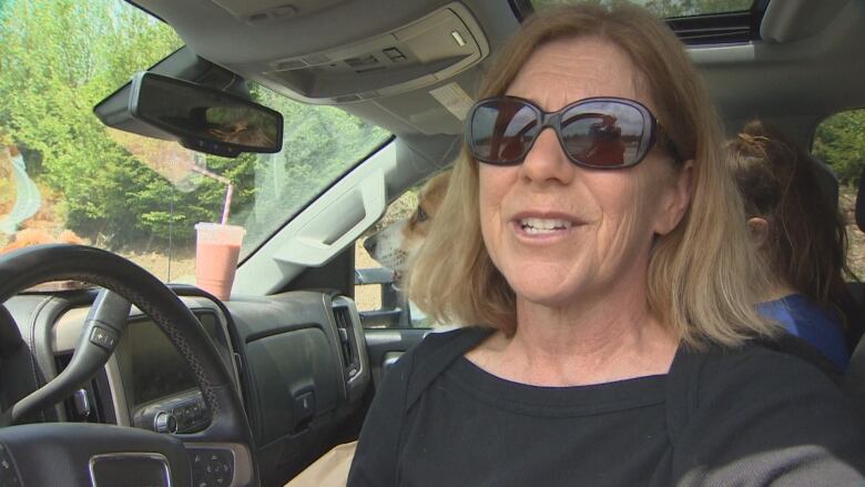 A woman in dark sunglasses speaks to the camera.